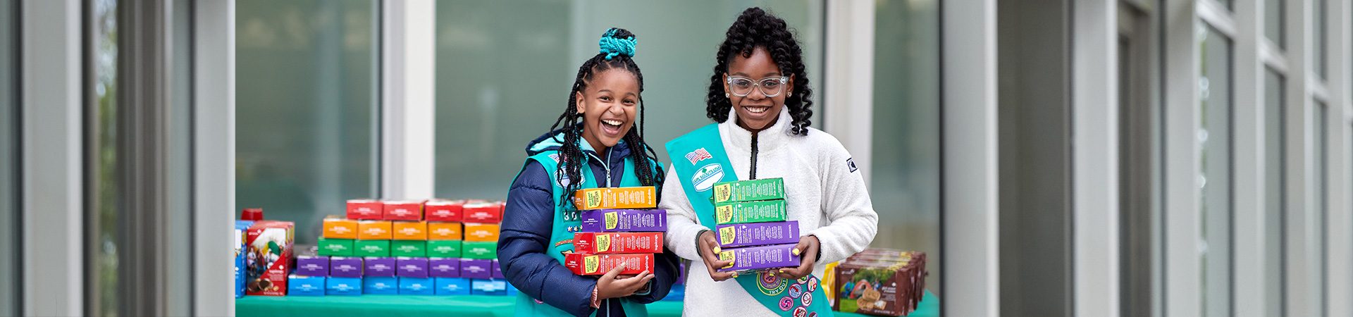  hands of young girl scout holding cookie boxes next to cookie transporter 